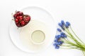 Matcha tea in a ceramic Cup on a white round plate with a knitted napkin and berries of ripe cherries in a heart-Cup and a bunch