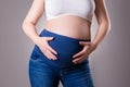 Maternity clothes, pregnant woman in blue jeans on gray background