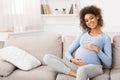 Happy pregnant woman sitting on sofa and caressing her belly Royalty Free Stock Photo