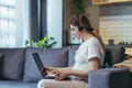 Maternity leave. Work. Pregnant freelancer woman sitting at home on sofa with laptop and in headphones in home clothes. Works on Royalty Free Stock Photo