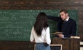 Math teacher pointing at green board. Professor giving explanations to brunette female student. Turn back girl in white Royalty Free Stock Photo