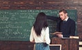 Math teacher pointing at green board. Professor giving explanations to brunette female student. Turn back girl in white Royalty Free Stock Photo