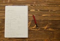 Notebook with red pencil on wooden table.