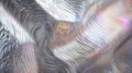 Mathematical wave interference patterns translated into physical texture rendered in metallic silver with holographic color shifts