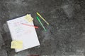 Mathematics book with calculation tasks, with orange, yellow and green pencil, shopping list and to do list post it on a grey