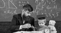 Mathematics lesson concept. Father teaches son mathematics. Teacher in formal wear and pupil in mortarboard in classroom Royalty Free Stock Photo