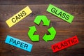 Matherials suitable for recycle near green recycle eco symbol. Words paper, glass, plastic, cans on dark wooden Royalty Free Stock Photo