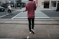 Person wearing purple long sleeved shirt and black pants walking on a sidewalk near zebra crossing