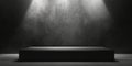 A matte black podium with a smooth surface, placed in front of a textured gray wall, lit by a Royalty Free Stock Photo
