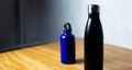 Matte black and shiny blue thermo bottles for water on wooden table.