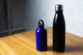 Matte black and shiny blue thermo bottles for water on wooden table.