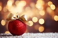 matte red Christmas ball with a gold bow on a snowy background of bokeh lights on a Christmas tree, copy space Royalty Free Stock Photo