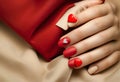 Matte red nails with small red heart on beige colour nail on the red fabric background. Saint Valentine\'s nail design