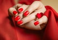 Matte red nails with small red heart on beige colour nail on the red fabric background. Saint Valentine\'s nail design