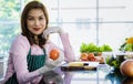 Matue adult Asian female housewife in apron sitting in kitchen holding fruit ready to make a vegetable healthy salad and looking Royalty Free Stock Photo