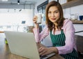 Matue adult Asian female housewife in apron sitting at table in kitchen holding glass of milk and ready to eat breakfast. Happy