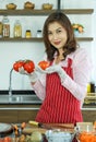 Matue adult Asian female housewife in apron standing in kitchen holding fruit ready to make a vegetable healthy salad and looking