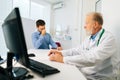 Mature adult male doctor explaining problem to crying sad young man patient sitting at desk during consultation at Royalty Free Stock Photo