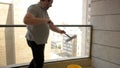 Man cleaning exterior decorative glass balcony aluminum fence with a double-sided telescopic mop
