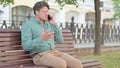 Mature Adult Man Getting Angry on Phone Call while Sitting on Bench