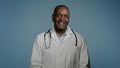 Mature african american man doctor stand in blue background studio in protective mask in medical gown takes off