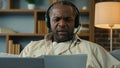 Mature african american man in headphones remote discuss with partner at online conference use laptop at home Royalty Free Stock Photo