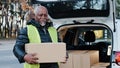 Mature african american smiling man holding cardboard box stands near open trunk of automobile happy elderly male Royalty Free Stock Photo