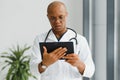 Mature african doctor using digital tablet in corridor . Portrait of confident male doctor using tablet computer in Royalty Free Stock Photo