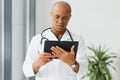 Mature african doctor using digital tablet in corridor . Portrait of confident male doctor using tablet computer in Royalty Free Stock Photo