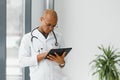 Mature african doctor using digital tablet in corridor . Portrait of confident male doctor using tablet computer in Royalty Free Stock Photo