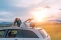 Mature age Man lying on car roof and reading the paper bestseller book. He stopped his auto on high grass meadow with beautiful