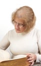 Mature age woman with glasses sits while reading old red paperback book Bible Royalty Free Stock Photo