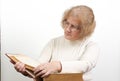 Mature age woman with glasses sits while reading old red paperback book Bible Royalty Free Stock Photo