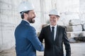 Mature architects in helmets shaking hands and smiling