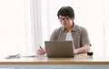 Mature Asian business man writing notes while working on laptop computer at his desk in home office. Entrepreneurship career, New Royalty Free Stock Photo