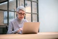 Mature asian business woman wears glasses using laptop computer sit at workplace desk Royalty Free Stock Photo