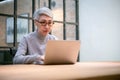 Mature asian business woman wears glasses using laptop computer sit at workplace desk Royalty Free Stock Photo