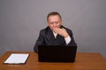 Mature Asian businessman sitting with wooden table against gray Royalty Free Stock Photo