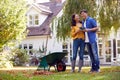 Mature Asian Couple Taking A Break With Hot Drinks Whilst Tidying Garden With Rake And Barrow