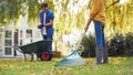 Mature Asian Couple Working In Garden At Home Raking And Tidying Leaves Into Barrow