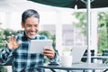 Mature asian man waving hand with smiling and enjoy using tablet making video call to child, grandchild or friends at outdoor Royalty Free Stock Photo