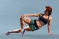 Mature athletic redhead woman doing fitness exercises, gray studio background