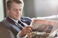 Mature attractive businessman reading newspaper while waiting and listening to music in airport