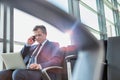 Mature attractive businessman talking on smartphone while sitting and working with his laptop before boarding in airport Royalty Free Stock Photo