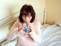 Mature attractive lady sitting on her bed using asthmatic pump spacer device to ease condition