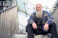 Mature bald hipster man with long beard sitting at footbridge in the city Royalty Free Stock Photo