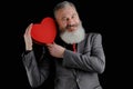 Mature bearded man wear suit holds red heart shaped gift box  isolated black background Royalty Free Stock Photo