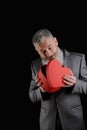 Mature bearded man wear suit holds red heart shaped gift box, isolated black background Royalty Free Stock Photo