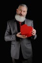 Mature bearded man wear suit holds red heart shaped gift box, isolated black background Royalty Free Stock Photo