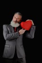 Mature bearded man wear suit holds red heart shaped gift box, isolated black background Royalty Free Stock Photo